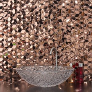 Rose gold faceted hexagon tile backsplash behind a crystal glass vessel sink.